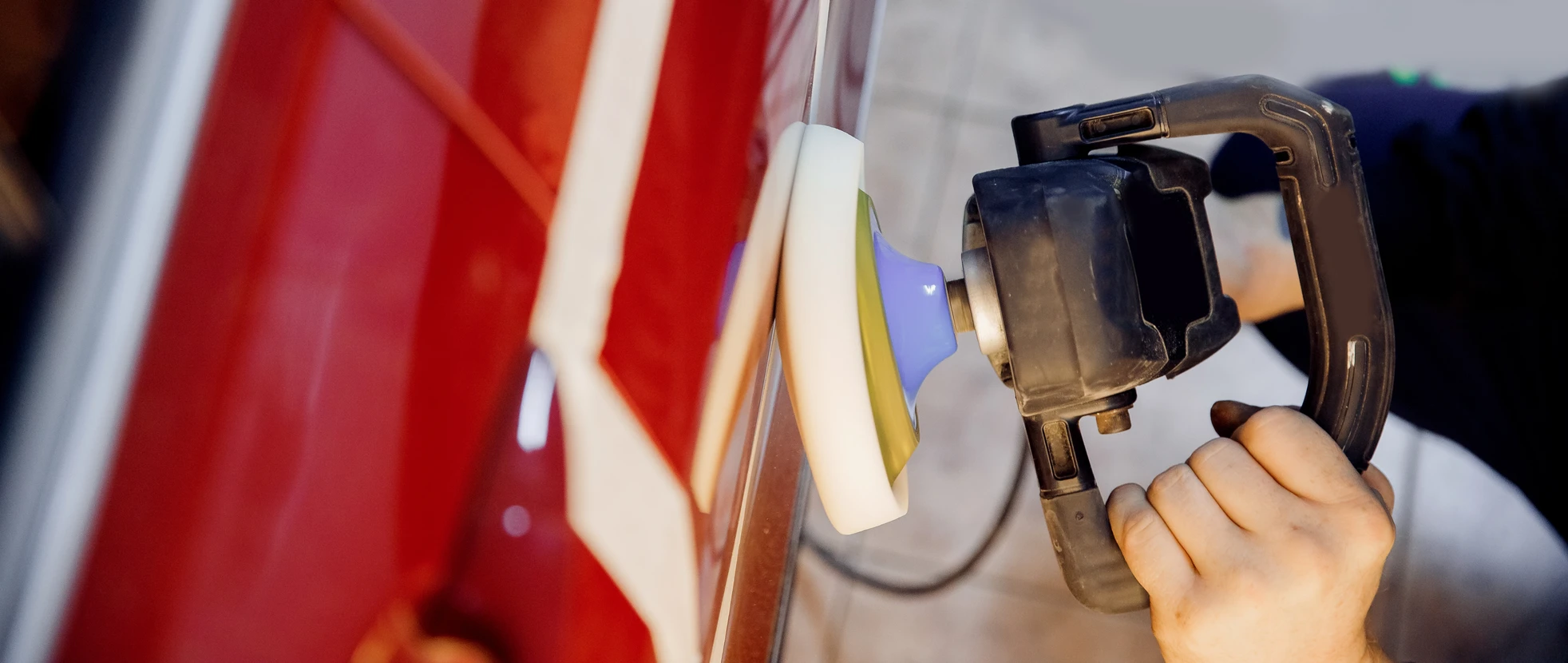 Intérieur atelier, main tenant une ponceuse orbitale électrique appliquée sur surface de carrosserie automobile rouge