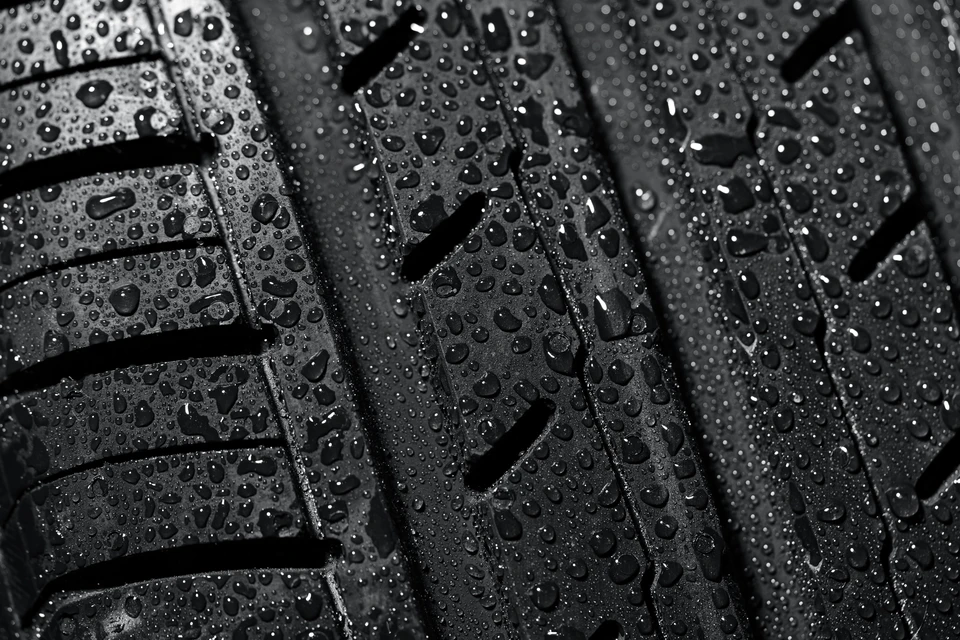 Pneu automobile noir avec bandes de roulement sculptées, couvert de gouttelettes d'eau sur toute sa surface