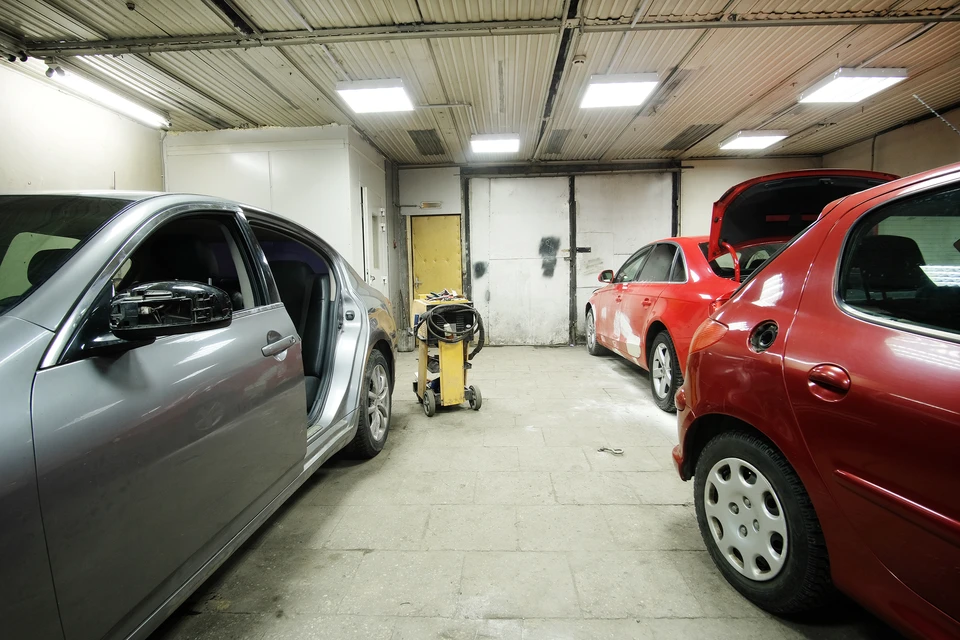 Int&eacute;rieur d'un garage automobile avec deux v&eacute;hicules en r&eacute;paration, une berline grise et une rouge avec capot ouvert