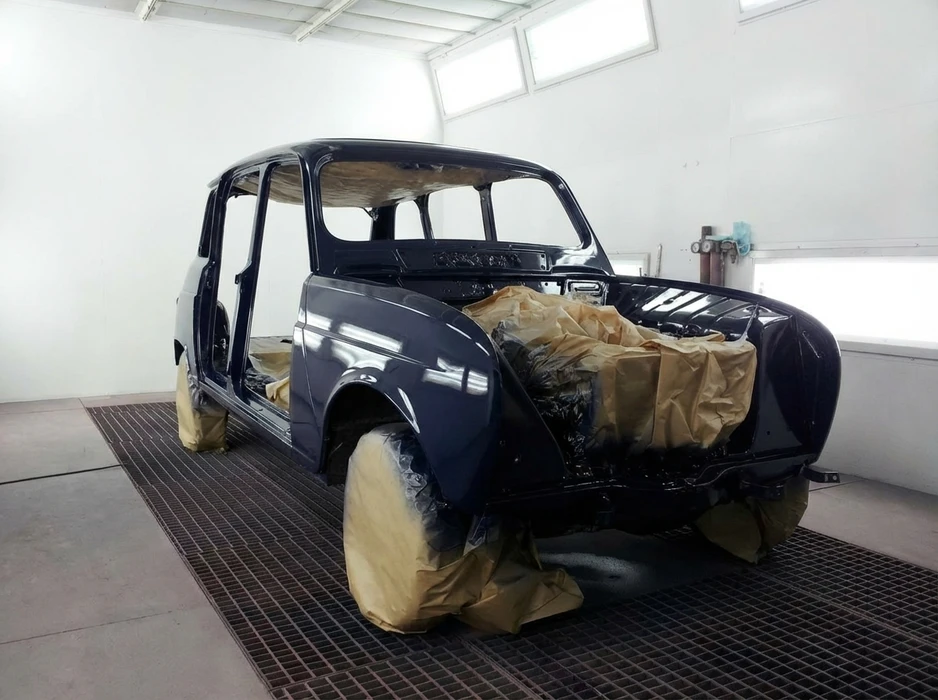 Carrosserie de voiture ancienne type berline compacte (Mini ou similaire) en cours de peinture en cabine pressurisée