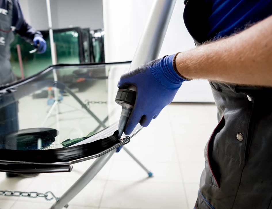 Scène extérieure en plein jour montrant deux techniciens en gants de protection bleus effectuant la réparation d'un pare-brise automobile