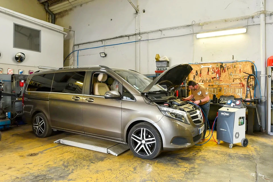 Deux techniciens en combinaison de travail bleue installent un pare-brise automobile dans un atelier de r&eacute;paration vitr&eacute;