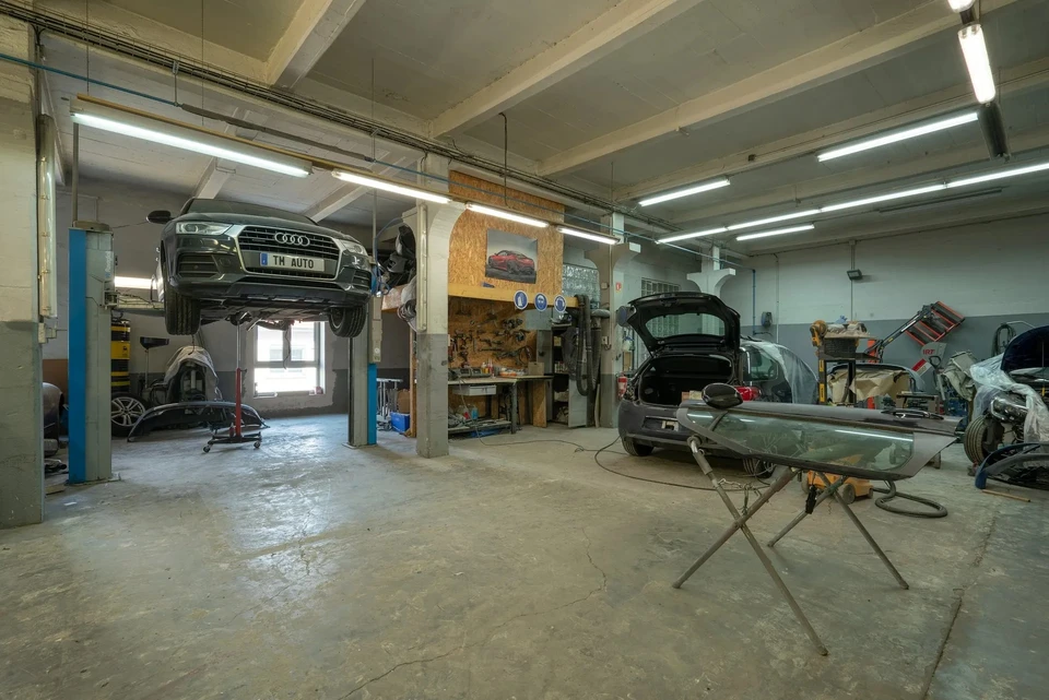 Atelier de réparation automobile avec technicien installant un pare-brise sur véhicule blanc
