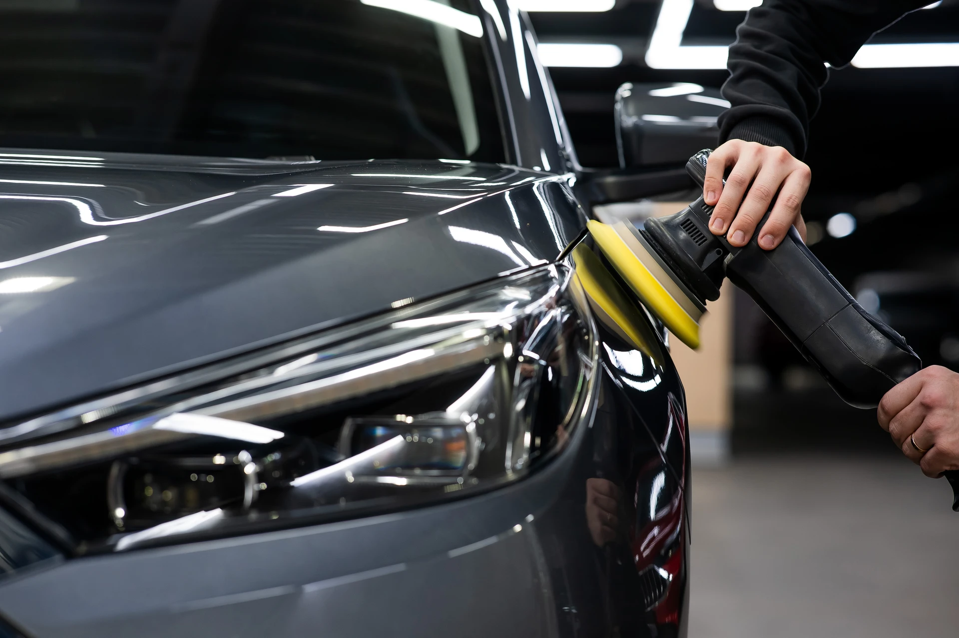 Atelier automobile intérieur avec technicien portant masque respiratoire et lunettes de protection appliquant peinture au pistolet sur carrosserie blanche de véhicule