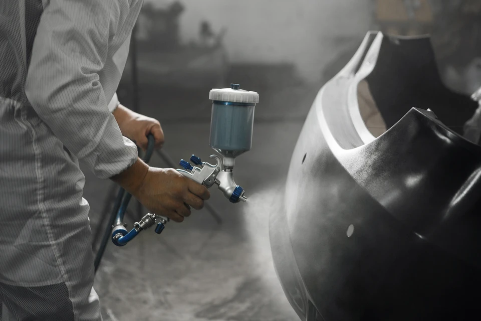 Atelier de réparation automobile moderne avec deux mécaniciens en combinaisons bleues examinant le moteur d'une berline grise, capot ouvert