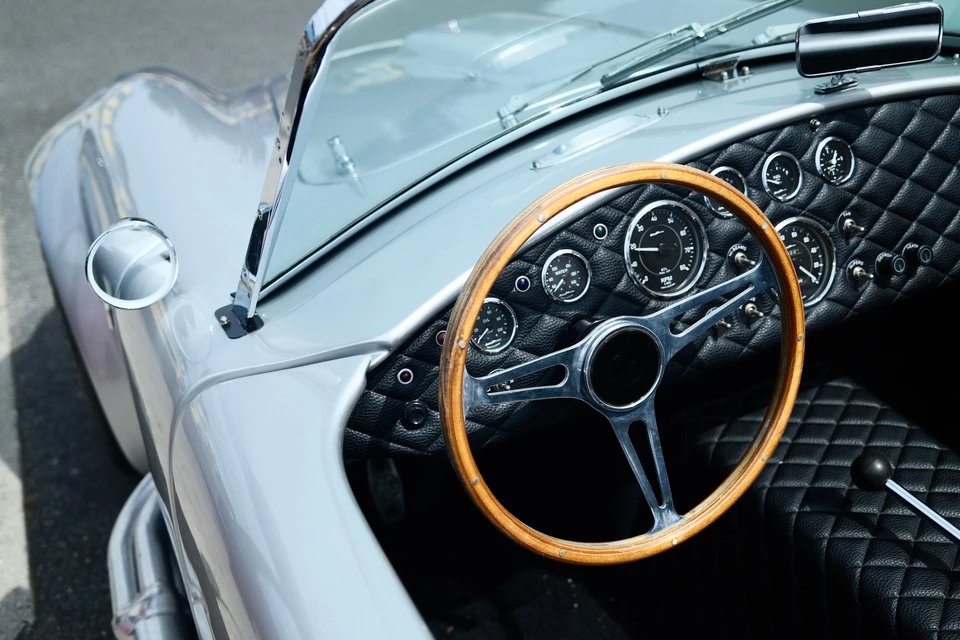 Intérieur d'une automobile de collection avec tableau de bord vintage en cuir rouge bordeaux, volant crème à trois branches, compteurs circulaires chromés avec cadrans noirs, autoradio d'époque