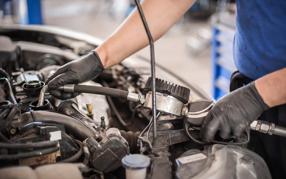 Atelier de réparation automobile intérieur avec mécanicien en combinaison bleue travaillant sous le capot ouvert d'une voiture blanche